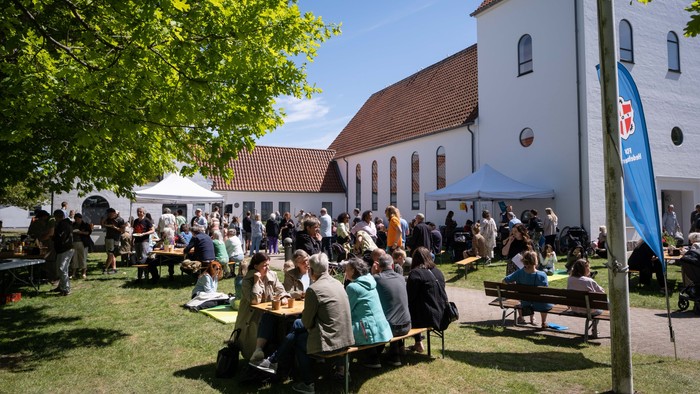 En folkemængde sidder og står ved en kirke, nogle spiser på bænke.