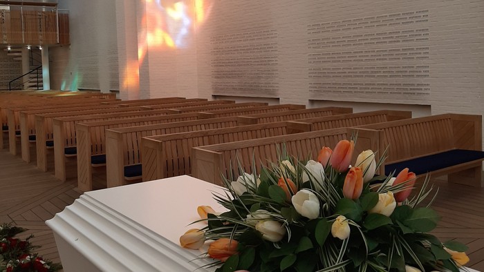 Kiste i Vejleå Kirke. Tulipaner på kisten, farvespil af lys på kirkens væg