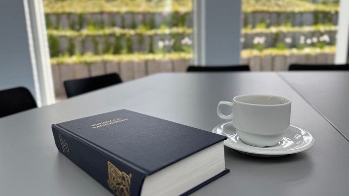 En bog og en teetasse på bord i et kontor med vinduesudsigt.