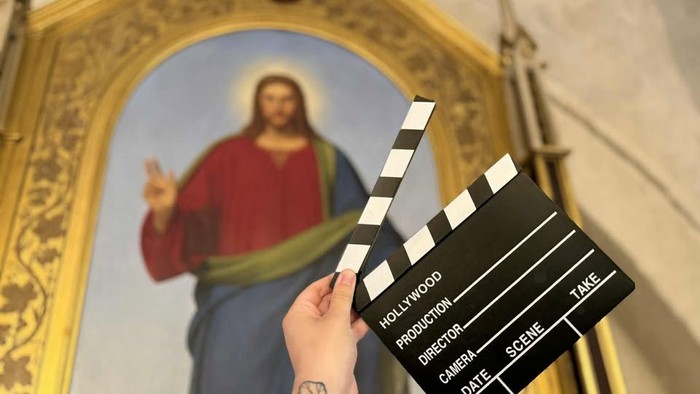 En person holder en klapplætte foran maleri af Jesus i en kirke.