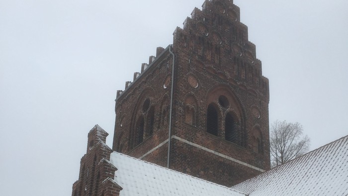 Gamle teglkirke med tårn og snødekt tag.
