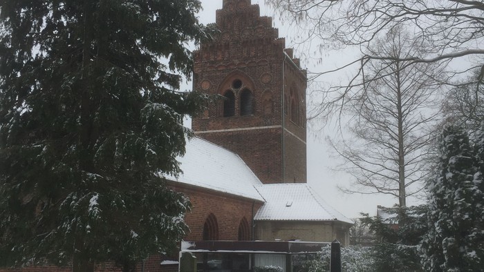 En snedækket kirke med tårn og en lille glasskulptur foran
