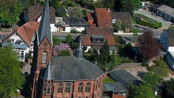 Ein Kirchengebäude mit hohem Turm inmitten eines Wohnviertels mit Häusern und Bäumen.