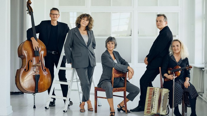 En gruppe musikere poserer med deres instrumenter i et lys og rummeligt rum