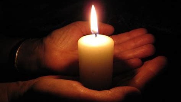 Sanfte Hände, die im Dunkeln eine brennende Kerze halten.