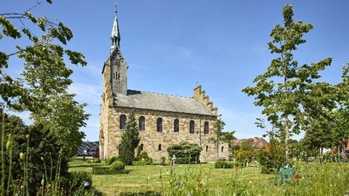 Kirche, blauer Himmel, im Vordergrund Wiese und Bäume