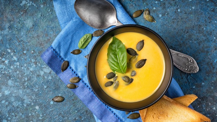 En bolle med gule suppe, pinde og grønne blade på blå duk og blå badekar.