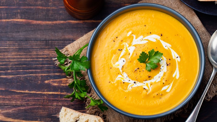 En bolle med gulerodsuppe med krem og grønne urter på et træbord