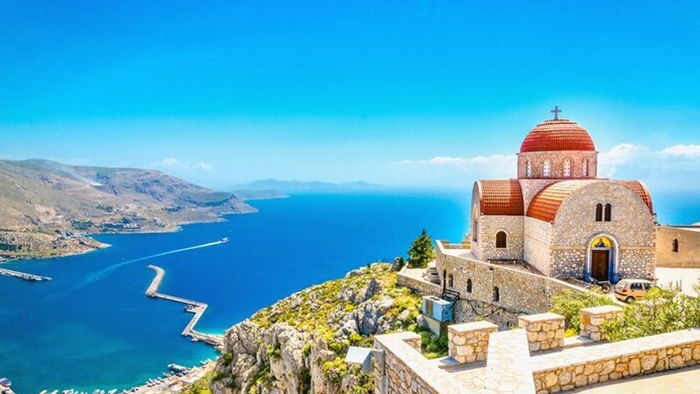 En malerisk kystkirke placeret på klipper med udsigt over et betagende, roligt blåt hav og fjerne bjerge.