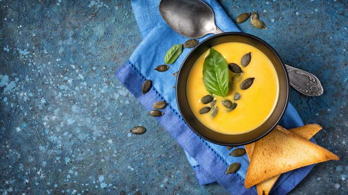 En bolle med gule suppe, pinde og grønne blade på blå duk og blå badekar.