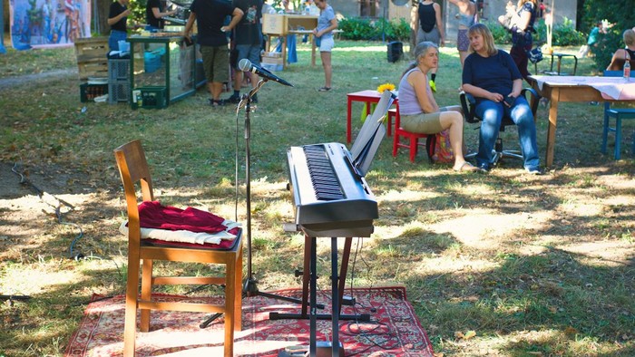 Im Garten wird Musik gemacht, Menschen sitzen und stehen um ein Klavier.