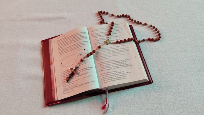 Geöffnetes religiöses Buch mit Rosenkranz und Kreuz, die auf den Seiten liegen.