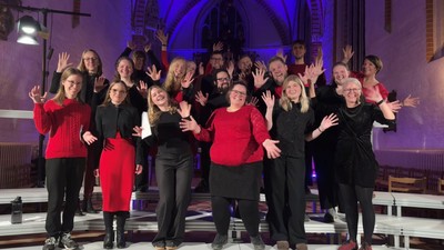 Gruppe af kvinder, der poser sammen på scenen, nogle iført røde og sorte outfits.