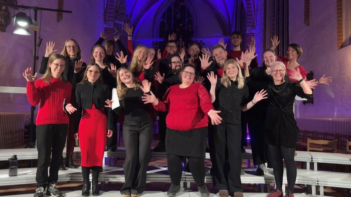 Gruppe af kvinder, der poser sammen på scenen, nogle iført røde og sorte outfits.