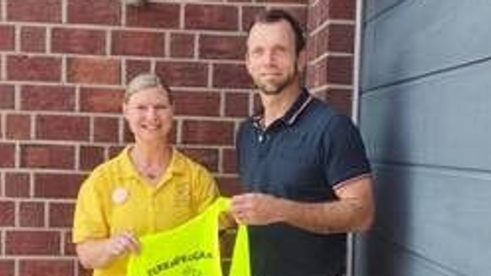 Zwei Personen stehen vor einer blauen Tür, eine hält eine gelbe Tasche.