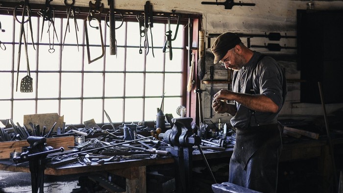Ein Mann arbeitet in einer Werkstatt mit verschiedenen Werkzeugen und Metallteilen.