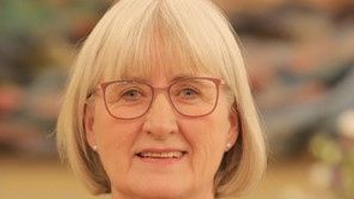 En smilende kvinde med blondt hår og briller har en blomstermønstret sort top på.