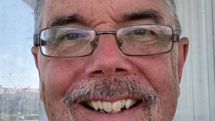 Middle-aged man with glasses and beard smiling.