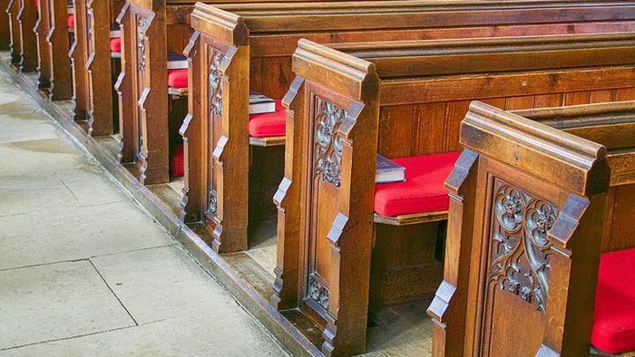 Wooden church pews with red cushions and taped off sections.