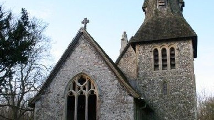 Quaint stone church with tall bell tower and arched windows set in a serene landscape.