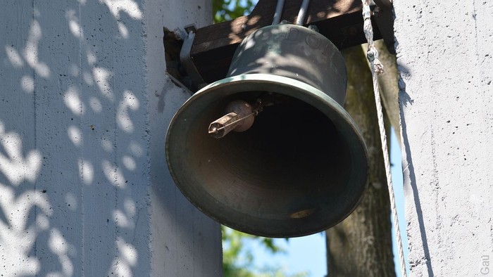Eine Glocke ist an der weißen Wand befestigt.