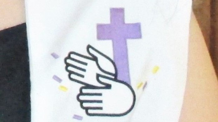 Ein weißes T-Shirt mit einem lila Kreuz und zwei Händen, die sich berühren