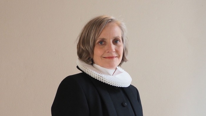 Kvinde i sort kaptajnmø, hvid krage og hvid kuffe.