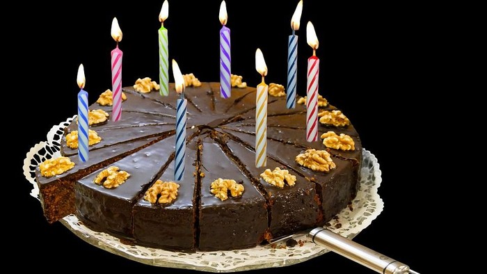 Ein reichhaltiger Schokoladenkuchen mit Walnüssen, beleuchtet von bunten Kerzen und mit einem Messer daneben.