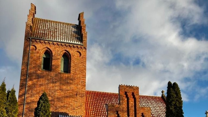 Røde murstenskirke med tårn og grøn dør.