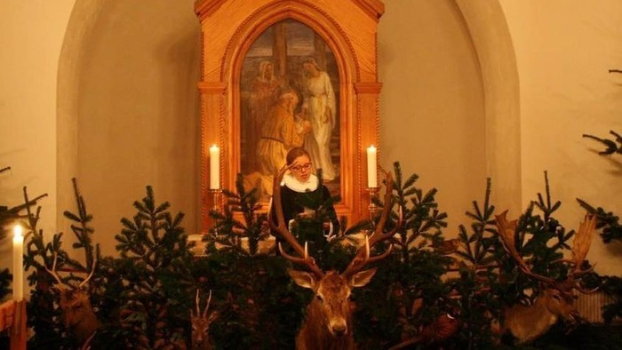 En kirkeindretning med skovfyr og candelabre foran et alterbillede