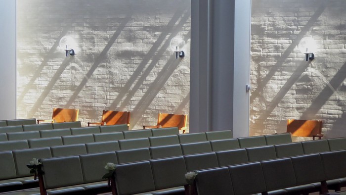 En flyveplads med grønne og orange stole forventende passagerer ved store vinduer med udsigt over en by.