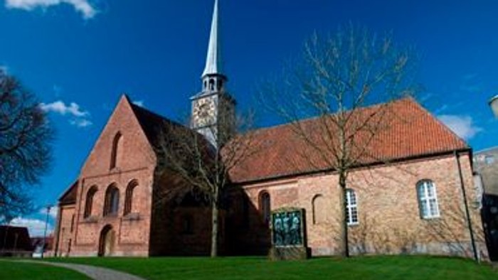 En rød murstenskirke med spir med tårn og træer foran