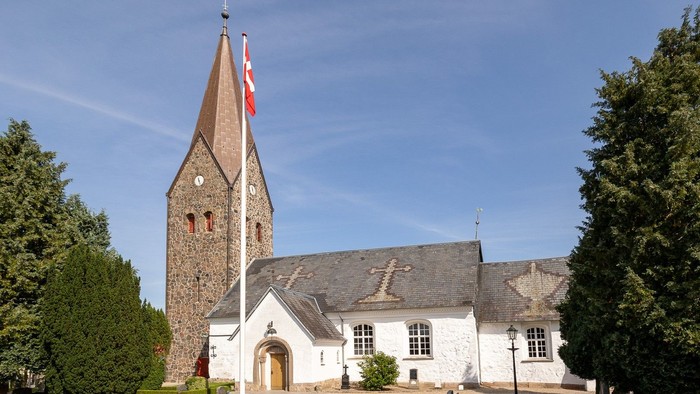 En hvid kirke med tårn og flag i et trædelt område