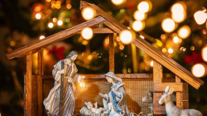 En julenisse med Maria, Josef, baby Jesus og dyr foran en juletree.