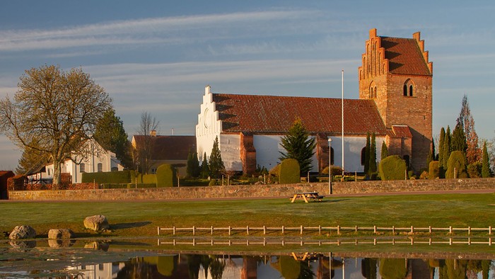 En rodfangst med en rød murstenskirke og træer, der reflekterer i en sø