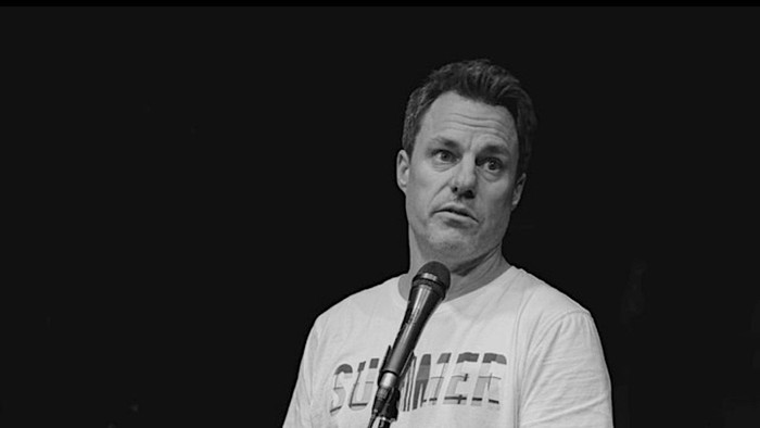 Mand står på scenen og holder mikrofon.