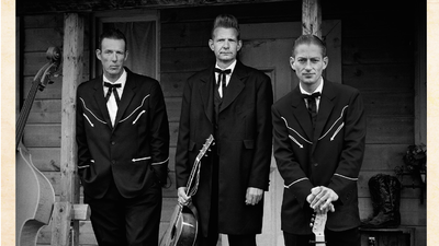 Tre mænd i formelle klæder med guitarer.