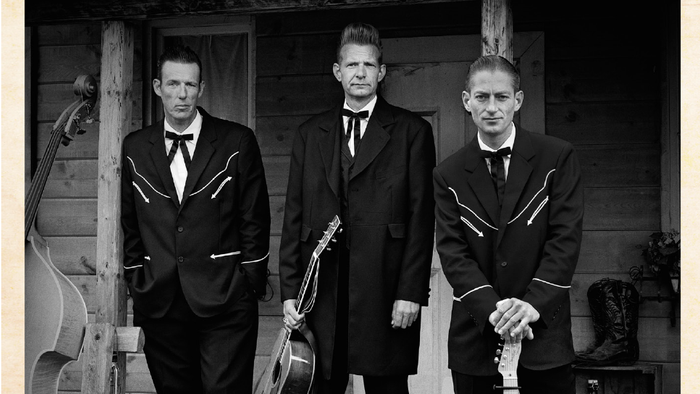 Tre mænd i formelle klæder med guitarer.