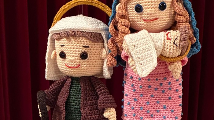 Hæklede dukker klædt ud som bibelske figurer med ruller, ophængt mod en rød baggrund.