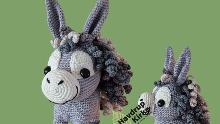 Håndstrikkede hækelæsser i form af æsler med farverige, fluffy maner og haler, udstillet på grøn baggrund.