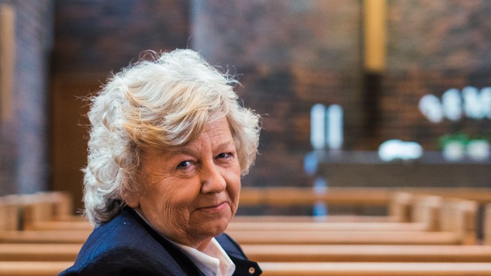 En kvinde sidder i en kirkebænk og smiler.