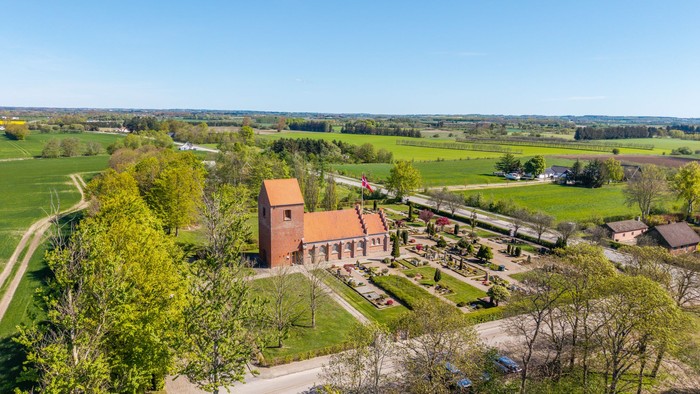 En stor rød murstenskirke i grønne landskab med vej og skov i nærheden