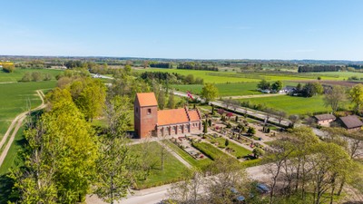 En stor rød murstenskirke i grønne landskab med vej og skov i nærheden