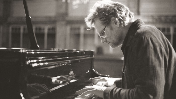 Mand spiller piano i et rum med store vinduer.