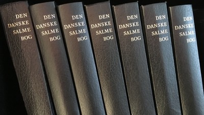Syv bind af "Den Danske Salmebog" på regals.