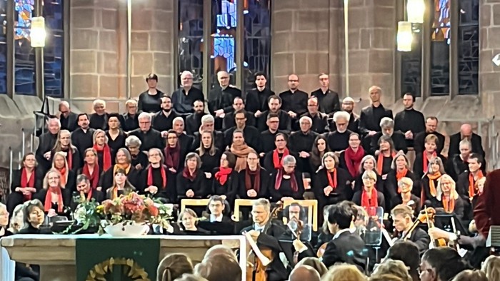 Ein großer Chor und ein Orchester treten gemeinsam in einer prächtigen, historischen Kirche während eines festlichen Konzerts auf.