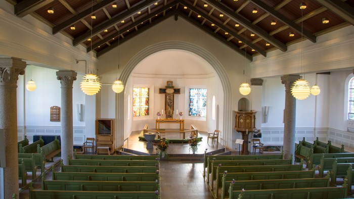 Indre del af kirke med grønne bænke og alter.