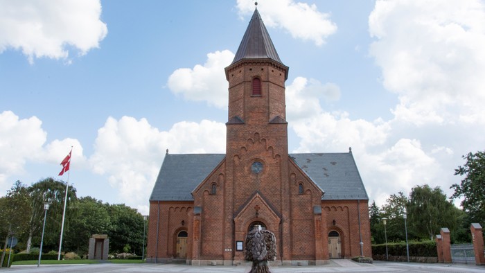 En rød murstenskirke med tårn og en fontæne foran
