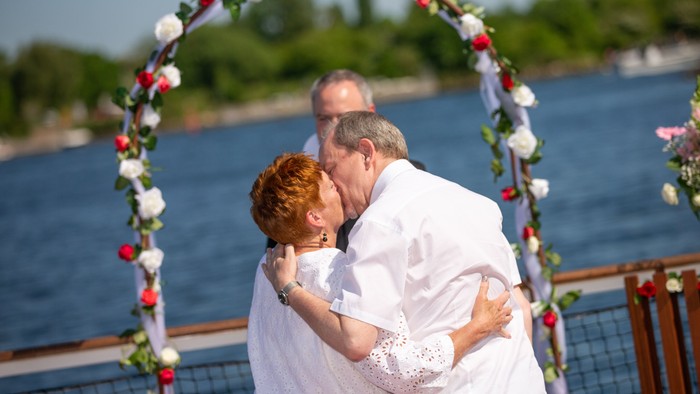 En bryllupspar kisser under en bukt med blomster ved vandet