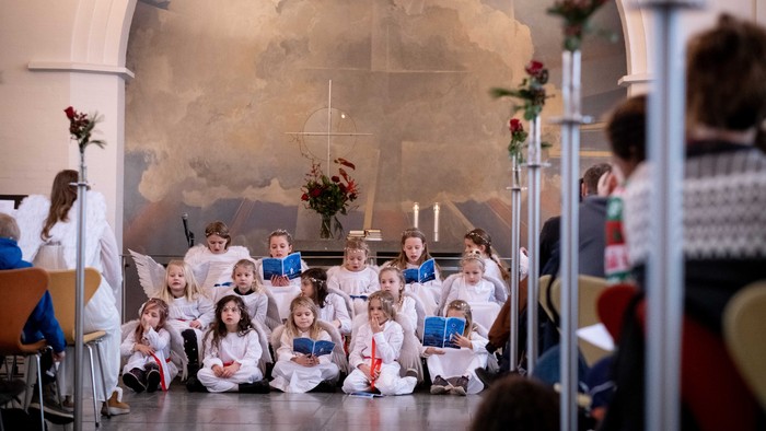 En gruppe børn synger i en kirke, alle med blå skjorter og hvide skjorter, og de holder blå bøger.